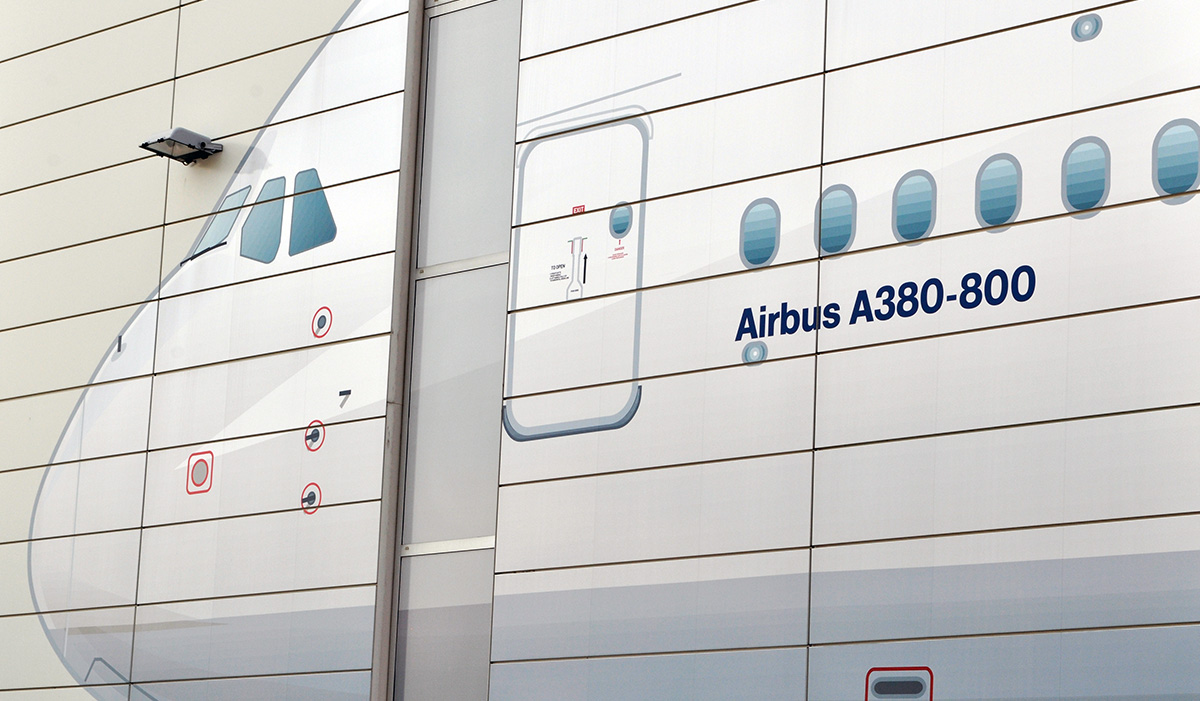 Stilisierte Wandbemalung eines Flugzeugrumpfs mit Notausstiegstür und Bullaugen-Fenstern auf einer weißen Hausfassade, im Corporate Design eines Airbus A380