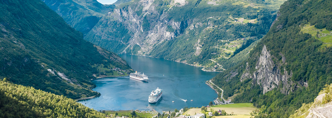 Luftaufnahme eines norwegischen Fjords mit Kreuzfahrtschiff, umgeben von steilen Felswänden und grüner Vegetation