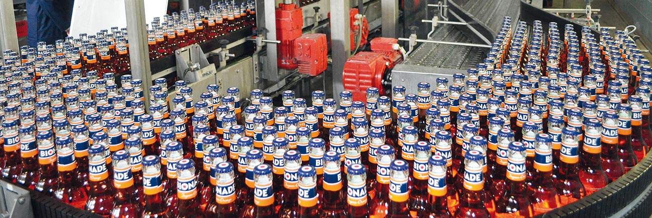 Bottling production line showing rows of Bionade bottles on a conveyor belt with industrial red machinery and equipment in the background.