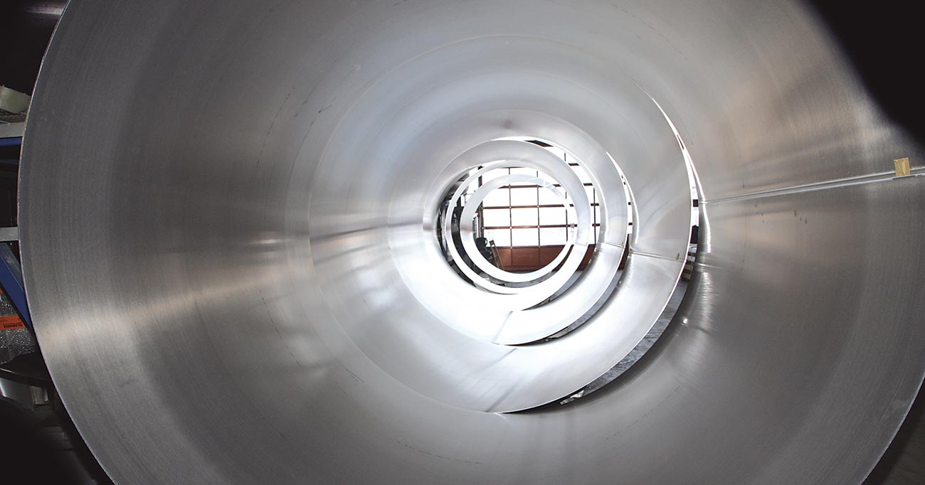 Blick in das Innere eines industriellen Silos aus Edelstahl mit spiralförmiger Tunnelstruktur und glänzender Metalloberfläche