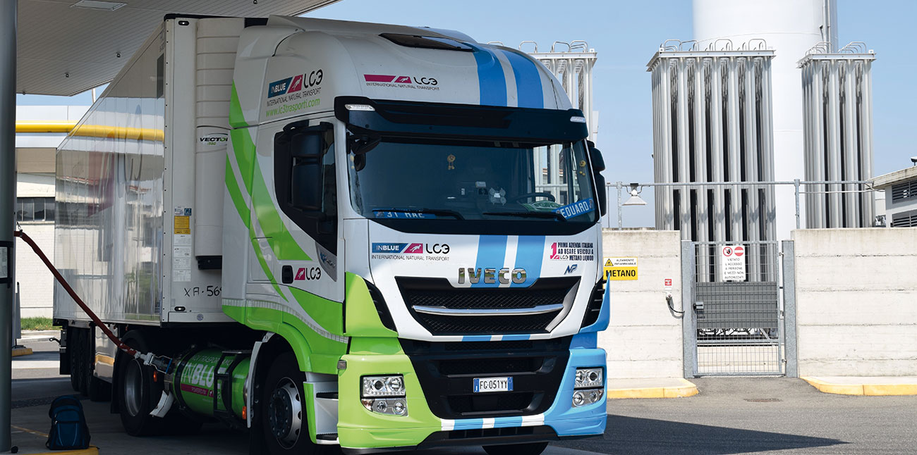 LKW parkt vor Industrieanlage mit Tanksäulen und Speichertanks, moderner Lastwagen in grün-blauem Design